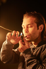 Obraz premium Young casual man with tobacco pipe in mouth holding lighter over its wide part