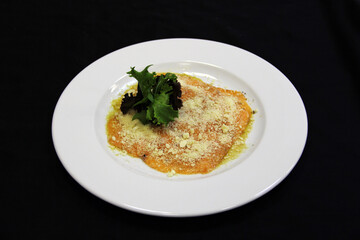 Red fish with lettuce leaves covered with grated cheese on a white plate