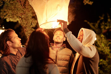 Young intercultural men and woman looking into illuminated large white balloon