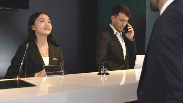 couple celebrating their anniversary checking in at hotel reception female receptionist asking for and checking their passports . He receives a key card from the room, business trip..