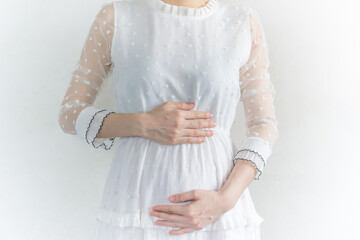Pregnant woman in dress holds hands on belly on a white background.
