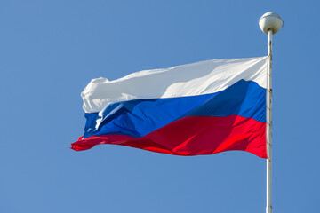 Russian flag on a flagpole against a blue cloudless sky