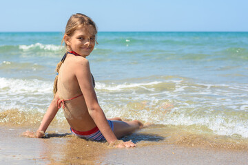 Fototapeta na wymiar The girl sits on a sandy beach and turned to look in frame