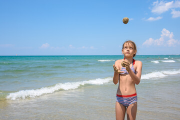 A girl of ten years juggles sand balls on the seashore