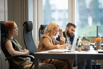 Fototapeta premium Happy mature businesswoman sitting by desk between two younger colleagues