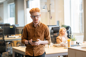 Young contemporary businessman in eyeglasses and casualwear using mobile phone