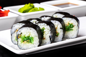 Roll with seaweed and sesame seeds on a white plate on a dark background. Sushi menu. Japanese food.