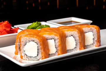 Roll with salmon and cheese on a white plate on a dark background. Sushi menu. Japanese food.