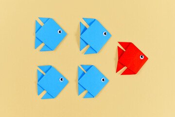 Red origami paper fish swimming in front of rows of blue fish. Concept for discovery and strong leadership.