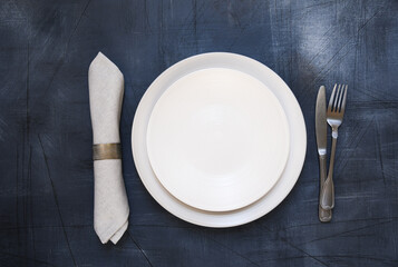 Table setting. White craft plate, cutlery and napkin on dark stone table. Top view, copy space,...