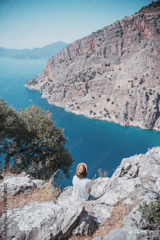 Wall mural Girl traveler in a hat looks from a cliff at the Oludeniz Butterfly Valley, traveling to Turkey