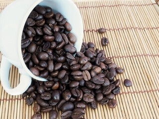 Coffee beans in a white glass And the coffee beans fell around on the wooden floor.
