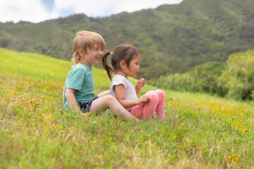 Fototapeta premium Two happy kids sitting on a large grassy hill on a hike