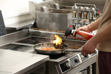Male chef with manual gas burner cooking tasty food on stove in restaurant kitchen, closeup of hands