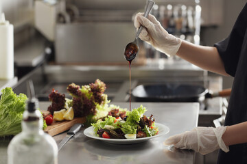 Female chef adding sauce to cooking food in restaurant kitchen, closeup