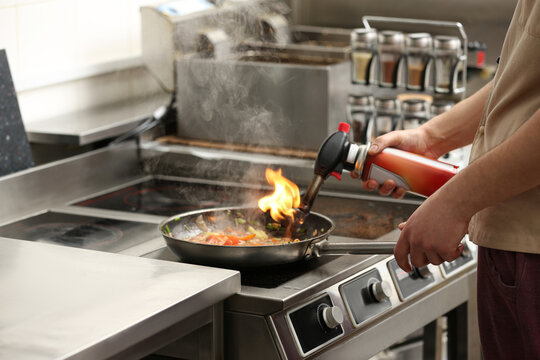 Male chef with manual gas burner cooking tasty food on stove in restaurant kitchen, closeup of hands