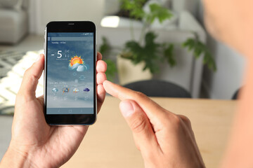 Man using weather forecast app  on smartphone indoors, closeup