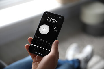 Man using weather forecast app on smartphone indoors, closeup