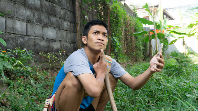 Asian man is gardening and thinking while looking at his cellphone