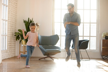 Happy father and adorable little daughter dancing in modern living room, spending free leisure time together at home, celebrating moving day, smiling dad and cute preschool girl enjoying activity