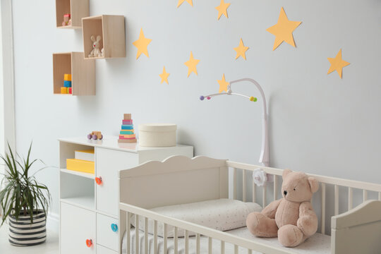 Crib with toy bear and mobile in stylish baby room interior © New Africa
