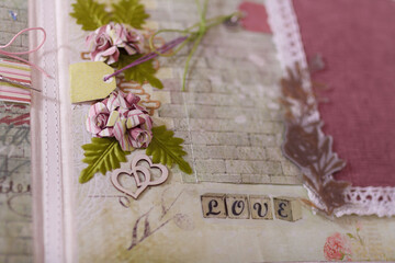 Soft focused close up shot of scrapbooking photo album page with paper decorative elements, flowers, hearts, lace. Leisure and hobby concept.