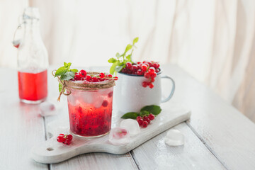 Glass of red currant cocktail or mocktail, refreshing summer drink with crushed ice and sparkling water on a white wooden background.
