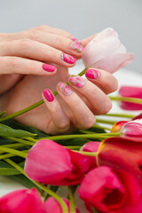 Close up vertical shot of woman hands with spring manicure holding pink tulip on tulips bouquet background. Nail art, gel nail polish design concept.