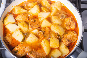 Cooking potatoes with chicken in a hot sauce, Italian cuisine - Arrabbiata garlic chicken with potatoes is cooked in a pan, close-up