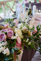 Beautiful floral arrangement of rose flowers and greenery on wedding table in restaurant, copy space. Luxury wedding decorations. Table setting