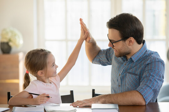 Happy little girl and father giving high five, studying at home together, smiling dad and pretty preschool girl satisfied by good homework results, homeschooling, teacher praising student