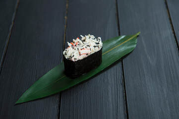 Close up of Japanese Gunkan Maki Sushi roll with snow crab and tobiko caviar on bamboo leaf on black wooden board. Background image cuisine concept. Traditional Pan Asian delicious restaurant menu
