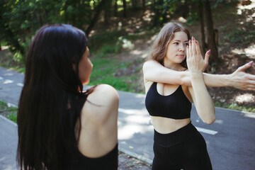 Friendship, personal trainer, group workout. Young fit women stretching hands during outdoor training. Active and healthy lifestyle