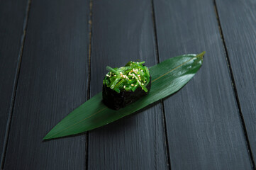 Close up of Japanese Gunkan Maki Sushi roll with Hiyashi wakame chuka and sesame seeds on bamboo leaf, wooden board. Traditional Pan Asian restaurant menu cuisine concept. Raw, vegan vegetarian food
