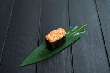 Close up of Japanese Gunkan Maki Sushi with salmon on bamboo leaf on black wooden board. Background image cuisine concept. Traditional Sake maki sushi roll. Pan Asian delicatessen restaurant food menu