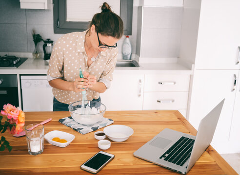 Beautiful Young Woman In Glasses Prepares Dessert In The Kitchen, Whips Whites And Dough, Cooking Class Online