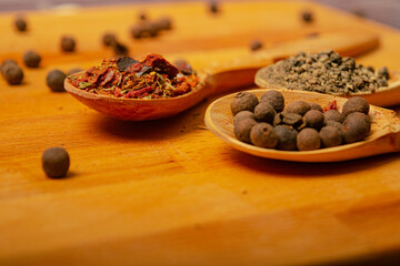 Black allspice, coarse salt and various ground spices in wooden spoons on a wooden Board. Close up.