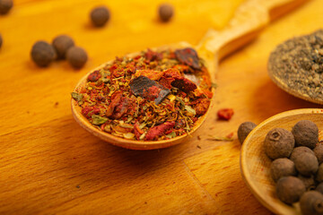 Black allspice, coarse salt and various ground spices in wooden spoons on a wooden Board. Close up.