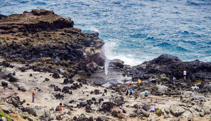 People standing around Nakalele Blowhole Geysir at rocky coast line or shore on North Maui Island...