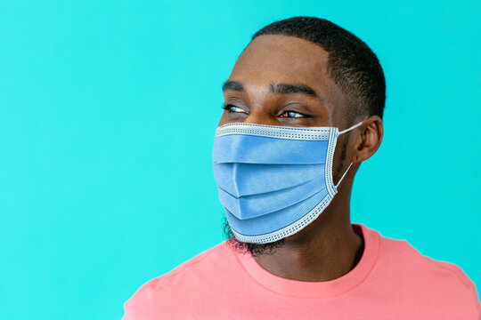 Portrait of a young african man wearing mask for coronavirus looking to side, against blue studio background