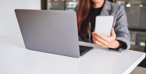 A beautiful young business woman holding and using mobile phone with laptop computer on wooden table