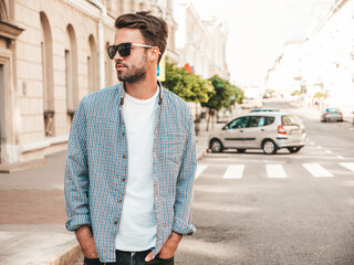 Portrait of handsome confident stylish hipster lambersexual model.Man dressed in white T-shirt. Fashion male posing on the street background in sunglasses