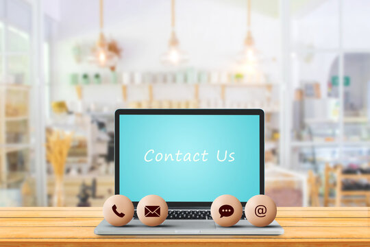 Call Center and Contact US Concept : Contact icons symbol put on laptop with blurry image of coffee cafe in background.