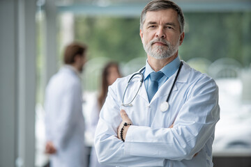 Confident smiling doctor posing in the hospital with medical team working on the background.