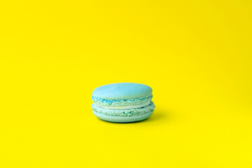 Close up view of tasty bright colored blue macaroon isolated on a bright yellow background. Sweet and colorful French macaroons. Dessert. Homemade sweets. Café dessert. Selective focus. Clipping path