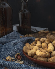 Table top of bar with brown bottles of beer, blue napkins or table cloth and raw peanuts in the shells in a bowl in the foreground.  Rustic dark and moody atmosphere with natural lighting