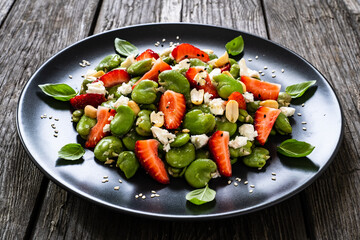 Broad beans salad with feta cheese and strawberries on wooden table
