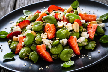 Broad beans salad with feta cheese and strawberries on wooden table
