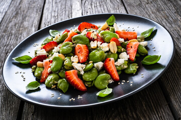 Broad beans salad with feta cheese and strawberries on wooden table
