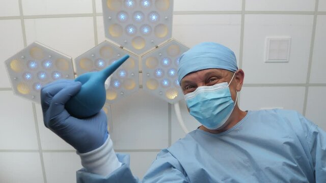 Doctor with an enema in his hands stands above the patient. Spiteful physician mocks patient in anticipation of medical procedure. Medical worker with enema